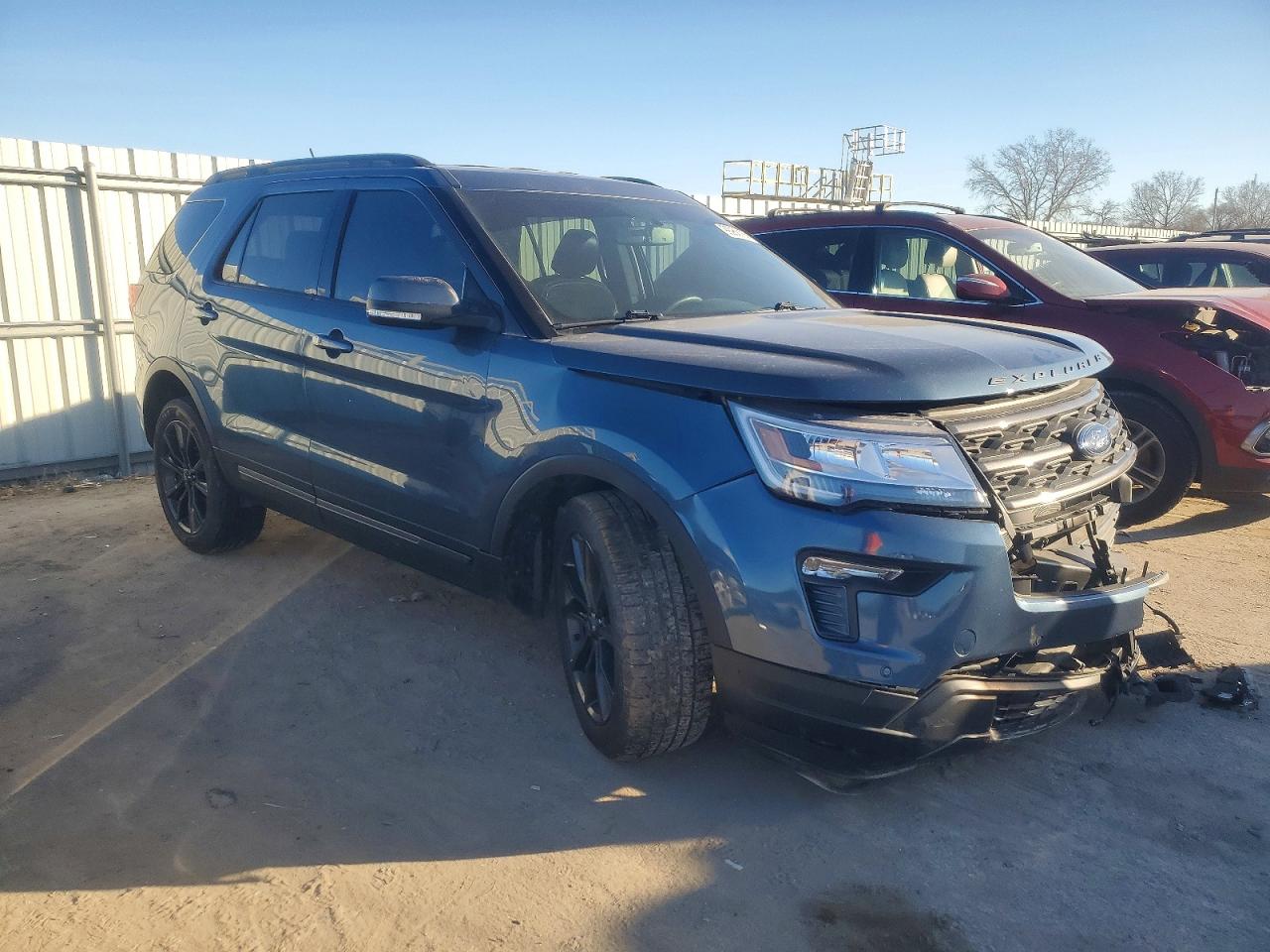 A dark blue 2019 Ford Explorer XLT SUV with side impact damage on rear passenger door and broken window parked on a city street