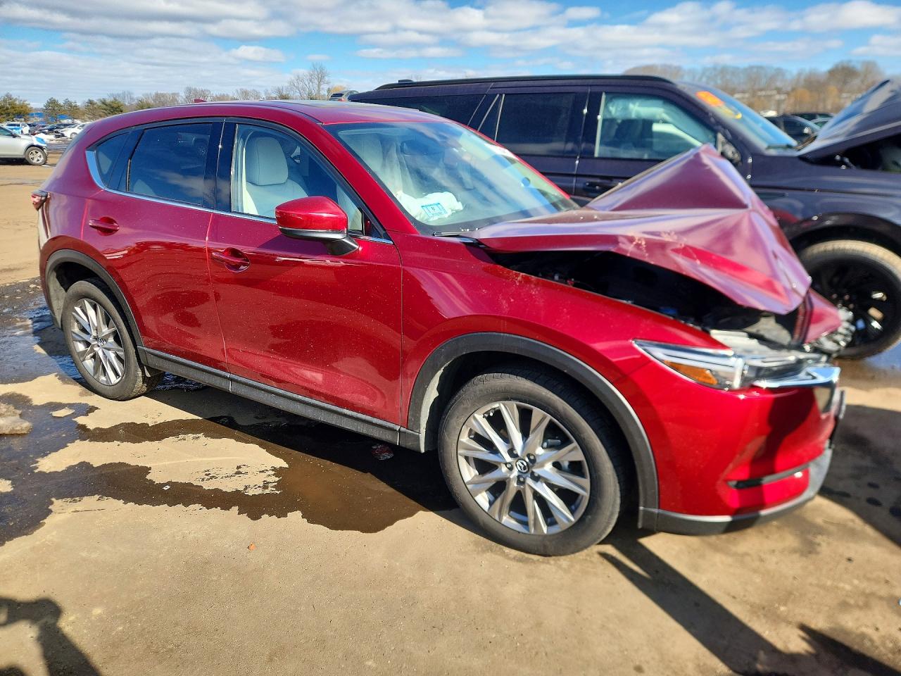 A dark gray 2020 Mazda CX-5 Grand Touring with rear-end collision damage and broken taillight at a body shop lot