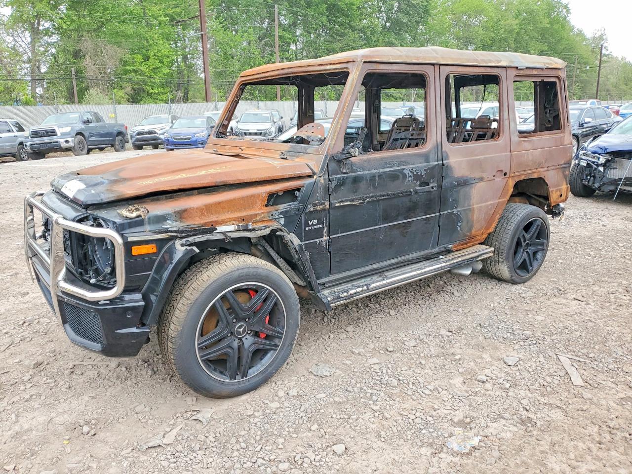 A black 2022 Mercedes-AMG G63 with front-end collision damage in a salvage yard at golden hour